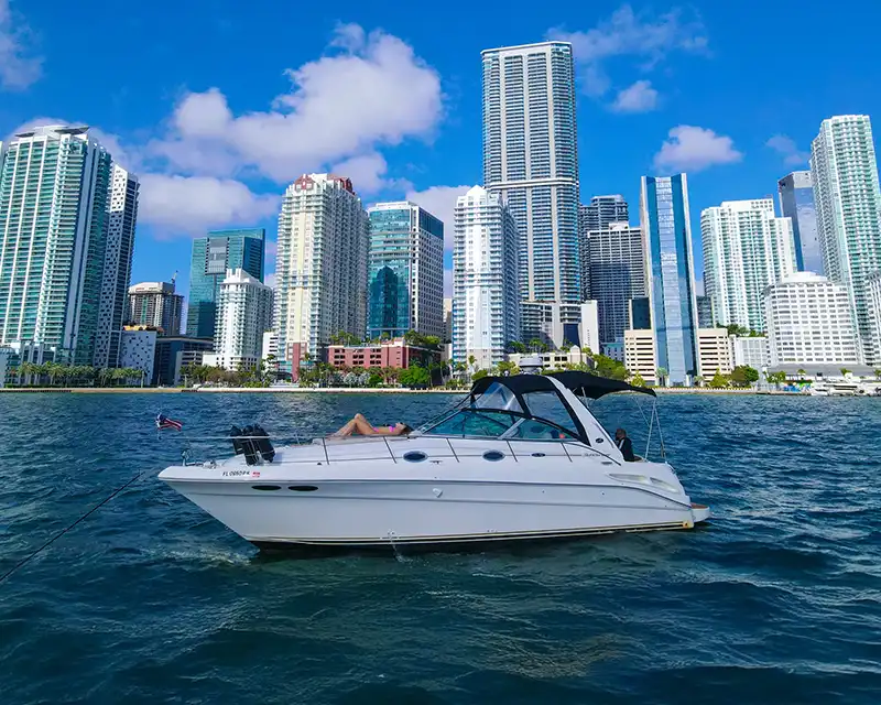White yacht on water with a city skyline background, under blue sky.